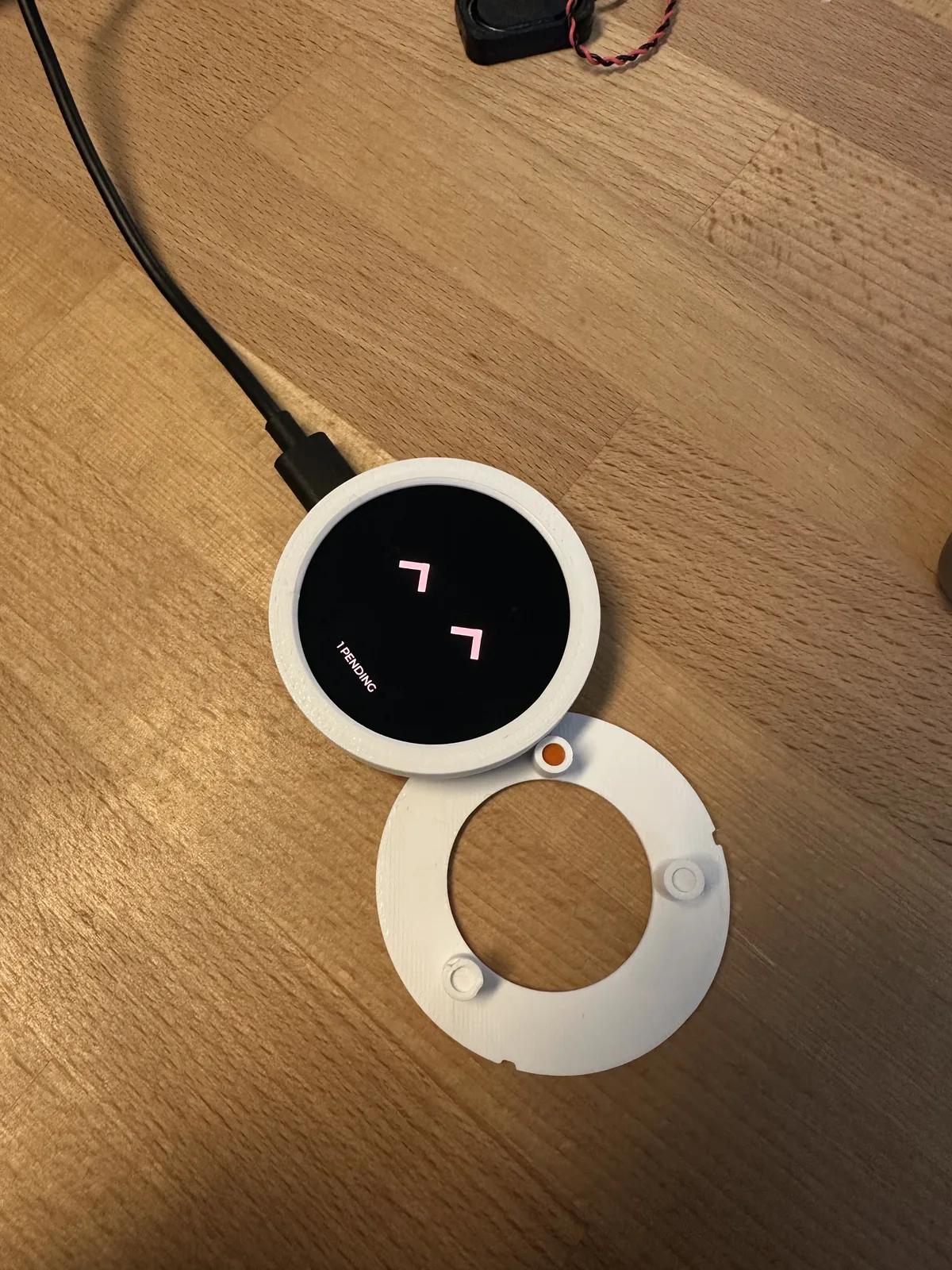 Powered round display in a white fit ring, beside a printed mounting plate on a wooden table
